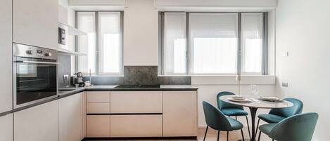 Una cocina moderna con electrodomésticos integrados, un comedor con sillas color turquesa y ventanas amplias que aportan luz natural.