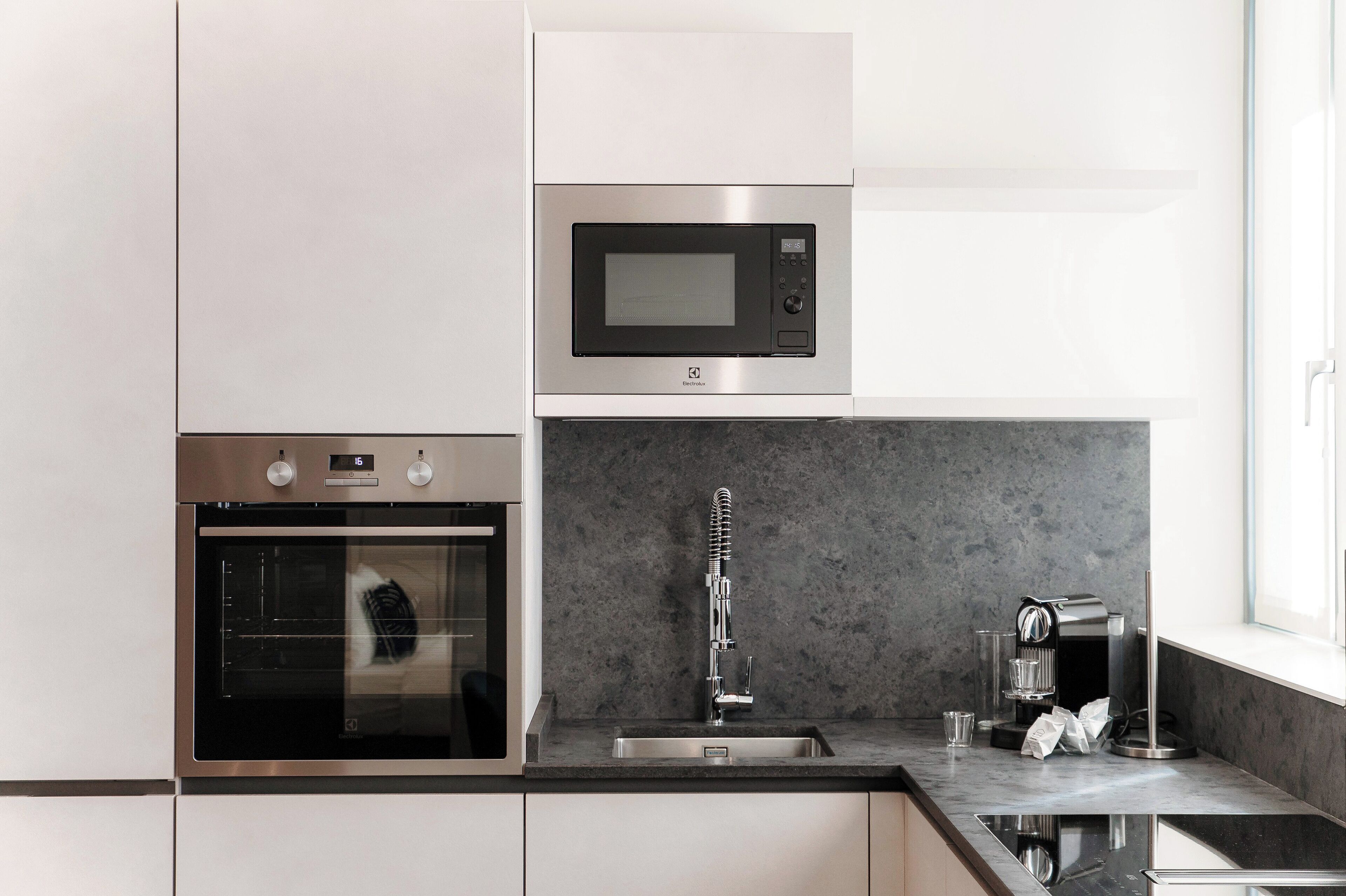 Cocina moderna con horno empotrado, microondas y grifo de acero inoxidable.