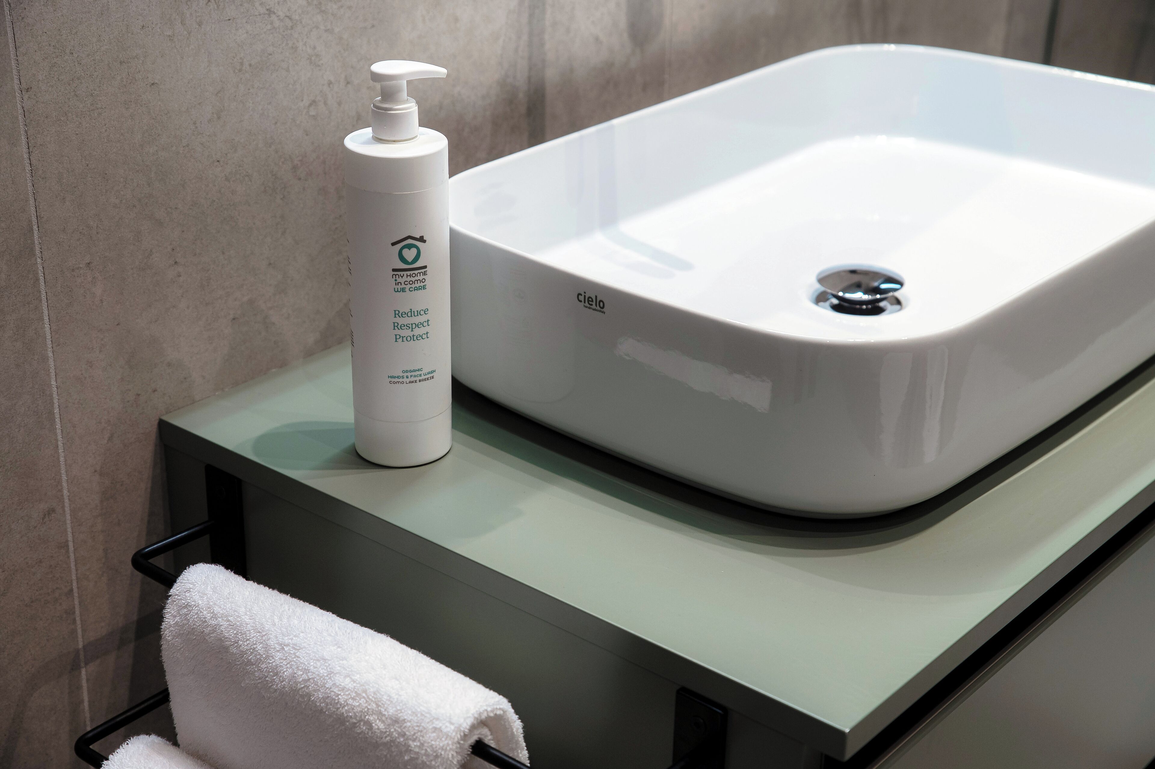 A bathroom with a white sink, a bottle of hand soap, and a white towel on a black towel rack.