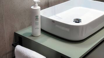 A bathroom with a white sink, a bottle of hand soap, and a white towel on a black towel rack.