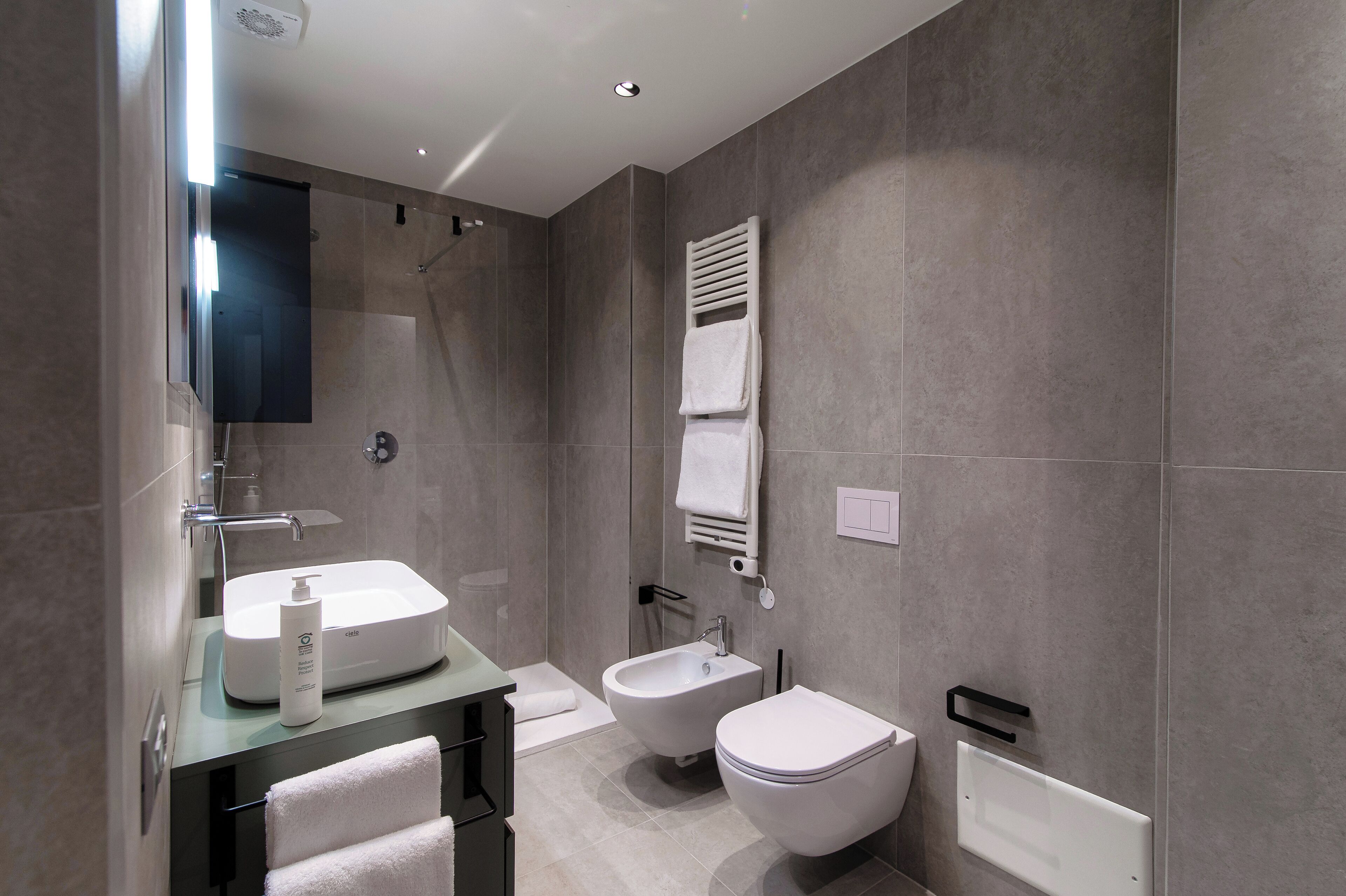 A modern bathroom with a glass-enclosed shower, a bidet, a toilet, and a vanity with a sink and towel rack.