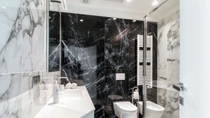 Casa de banho moderna com toucador de mármore, bidé e zona de duche com divisória de vidro.