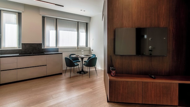 Uma cozinha moderna com área de jantar, armários de madeira e uma TV de tela plana fixada numa parede de madeira.