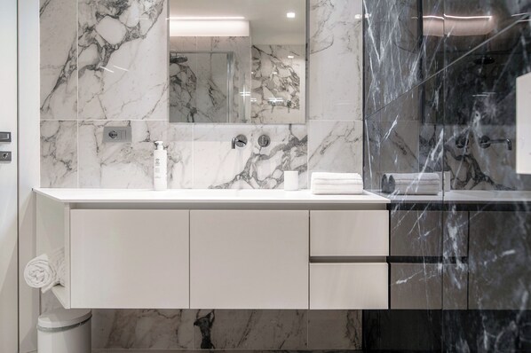 Une salle de bain moderne avec des murs en marbre, un meuble-lavabo blanc et une cabine de douche en verre.