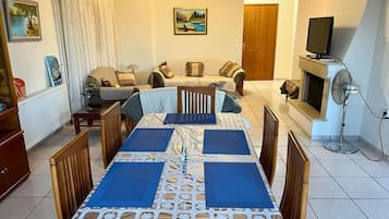 A dining area with a table set for four, a sofa in the background, and a television on a stand.