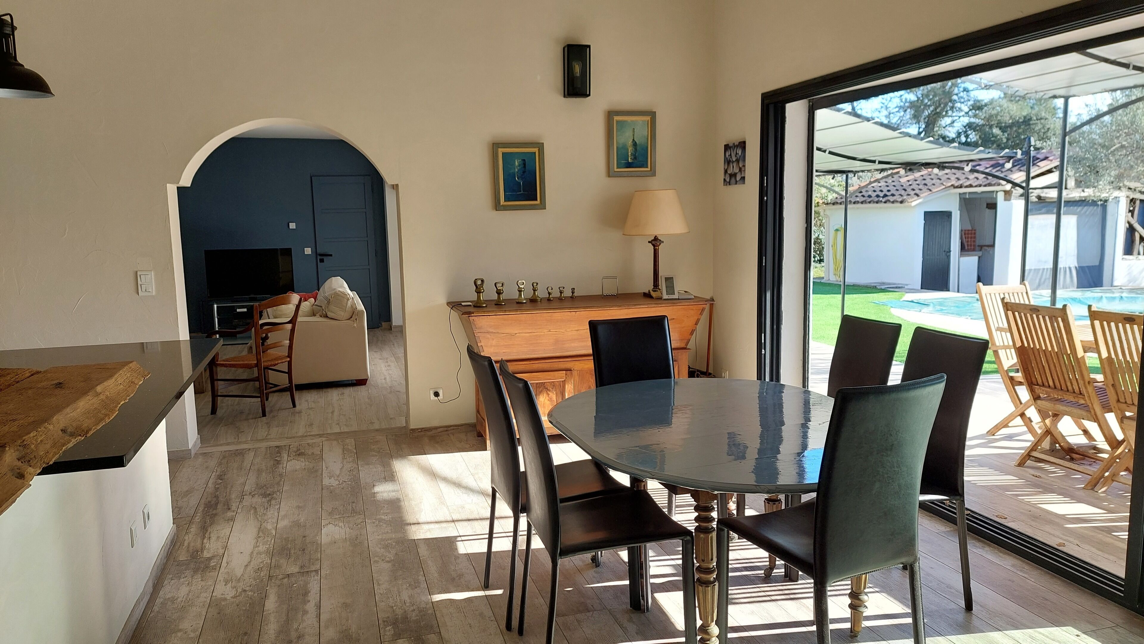 Un coin repas avec une table ronde et des chaises, une cuisine avec une porte bleue et une vue sur une piscine.