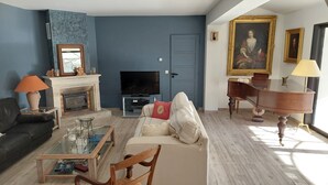 A living room with a sofa, a coffee table, a television, a fireplace, and a piano.