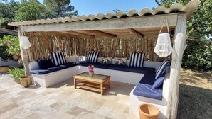 A covered outdoor seating area with a wooden bench, a table, and a potted plant.