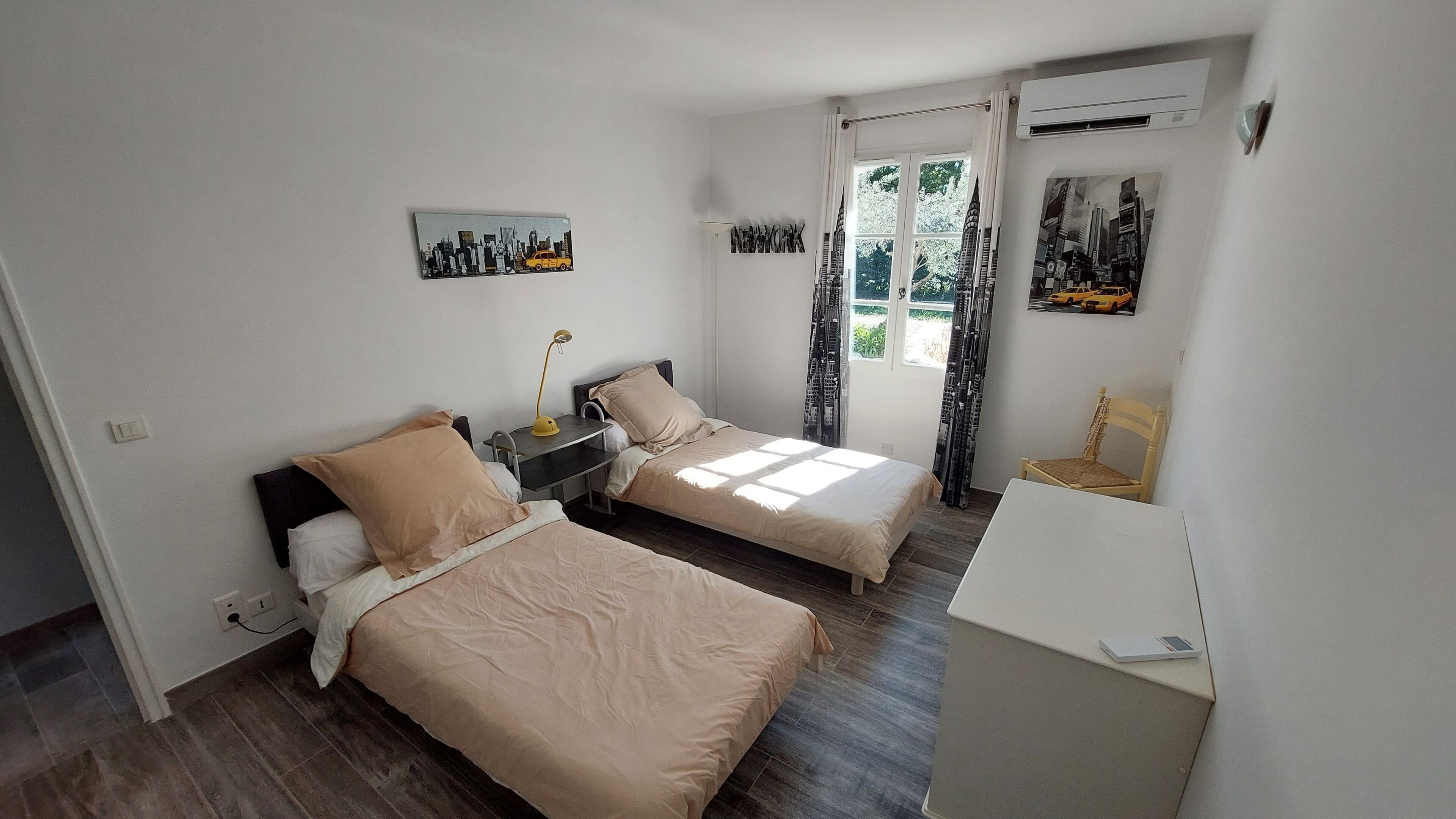 Ein Hotelzimmer mit zwei Betten, einem Schreibtisch, einem Stuhl und einem fensterbepflanzten Fenster.