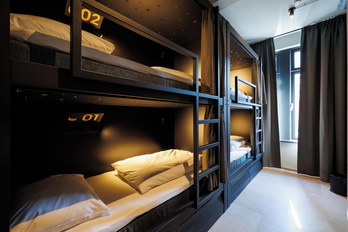 A bunk bed room with numbers on the beds, a ladder, and a window with curtains.