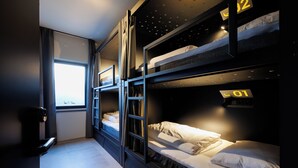 A bunk room with three levels, each marked with a number. There is a window providing natural light, and a door on the left side.