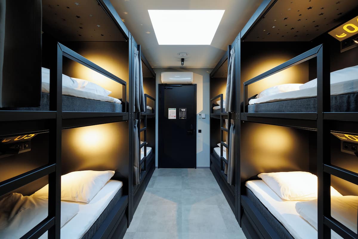 A narrow corridor with bunk beds on either side, a central door, and a skylight above.