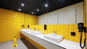 A restroom with three sinks, yellow tiled walls, and a caution sign on the floor.