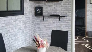 Ein Essbereich mit Backsteinwand, einem an der Wand befestigten Fernseher, einem kleinen dekorativen Gegenstand und einem Tisch mit Stühlen.