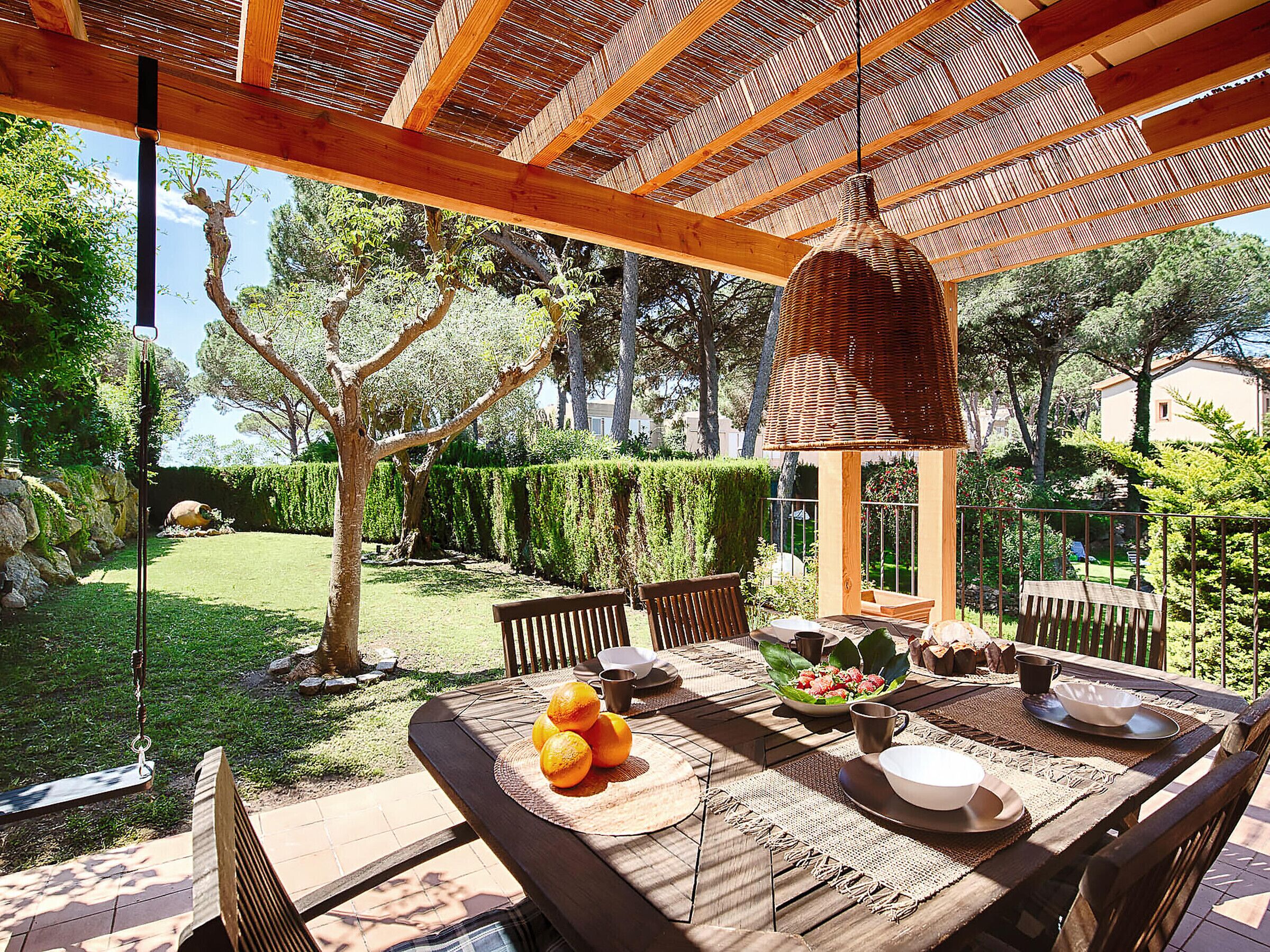 An outdoor dining area with a wooden table, chairs, and a hanging light fixture.