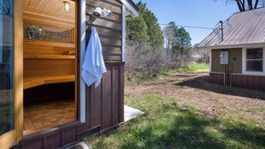 Una baita di legno con un'ampia porta aperta, un asciugamano appeso al manico e una piccola struttura adiacente con una finestra.
