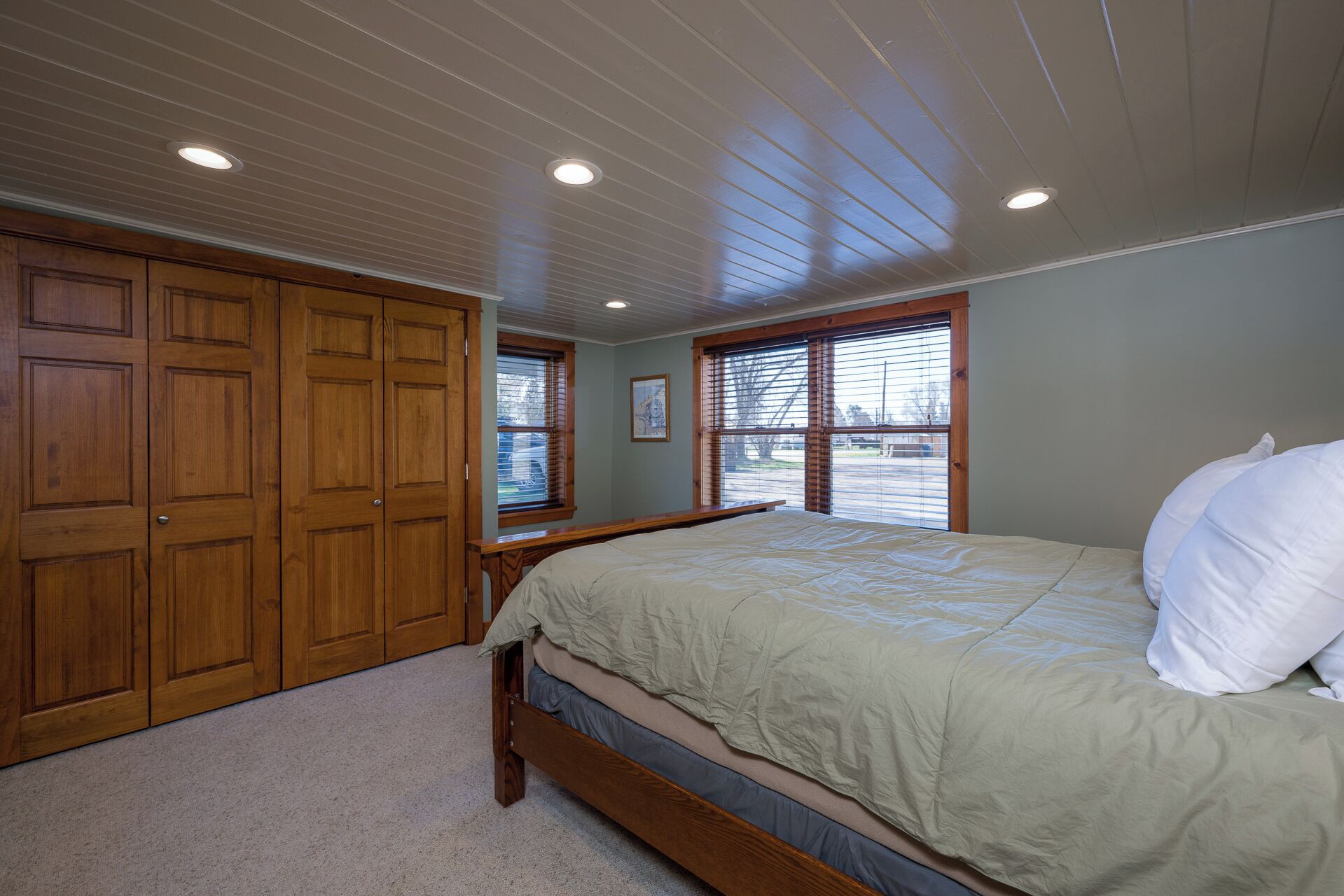 A bedroom with a bed, wooden wardrobe, and a window with blinds.