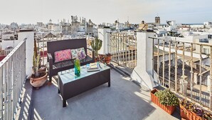 Une terrasse sur le toit avec un canapé en osier, une table basse en verre et des plantes en pot.