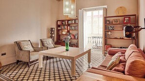 Un salon avec un sol à carreaux, une table blanche, un canapé marron et une bibliothèque remplie de livres et d’objets décoratifs.