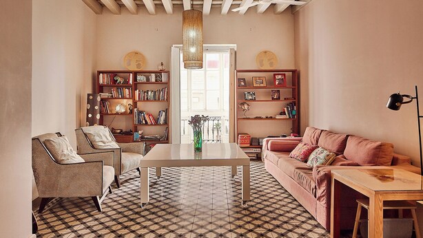 Un salon avec un sol à carreaux, un canapé, un fauteuil, une table basse et deux étagères remplies de livres et d’objets décoratifs.