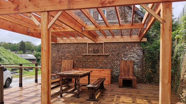 An outdoor wooden deck with a brick wall backdrop, wooden benches, a table, and a fire pit.