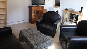 A living room with a black leather sofa, a matching ottoman, a wooden cabinet with a television, and a fireplace with a decorative mantel.