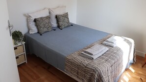 A neatly made bed with a blue bedspread and a patterned blanket, two pillows, and a folded towel on the side.