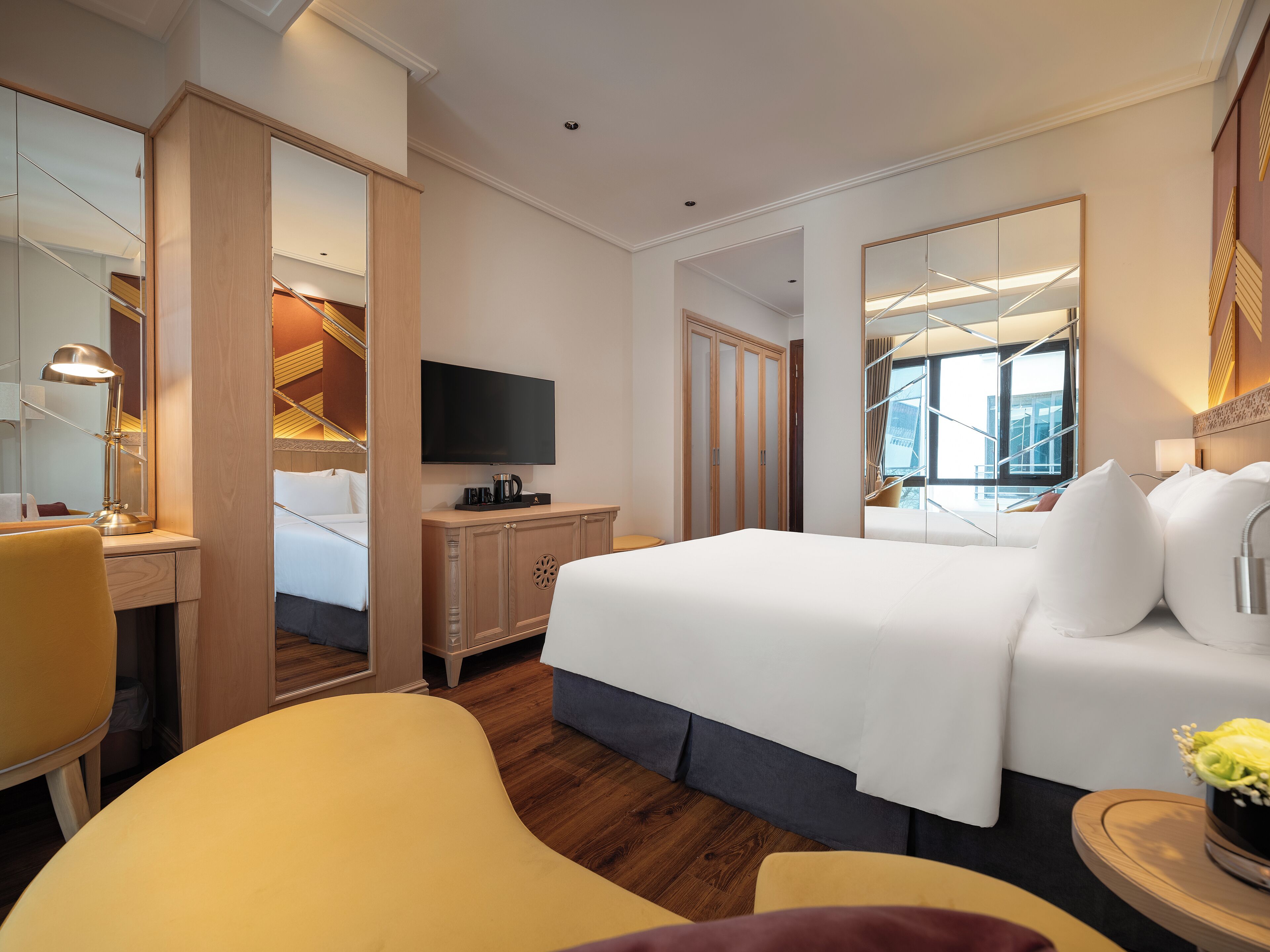 Quarto de hotel com uma cama grande, uma escrivaninha com abajur, televisão e vista da cidade pela janela.