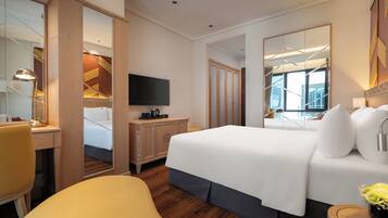 Quarto de hotel com uma cama grande, uma escrivaninha com abajur, televisão e vista da cidade pela janela.