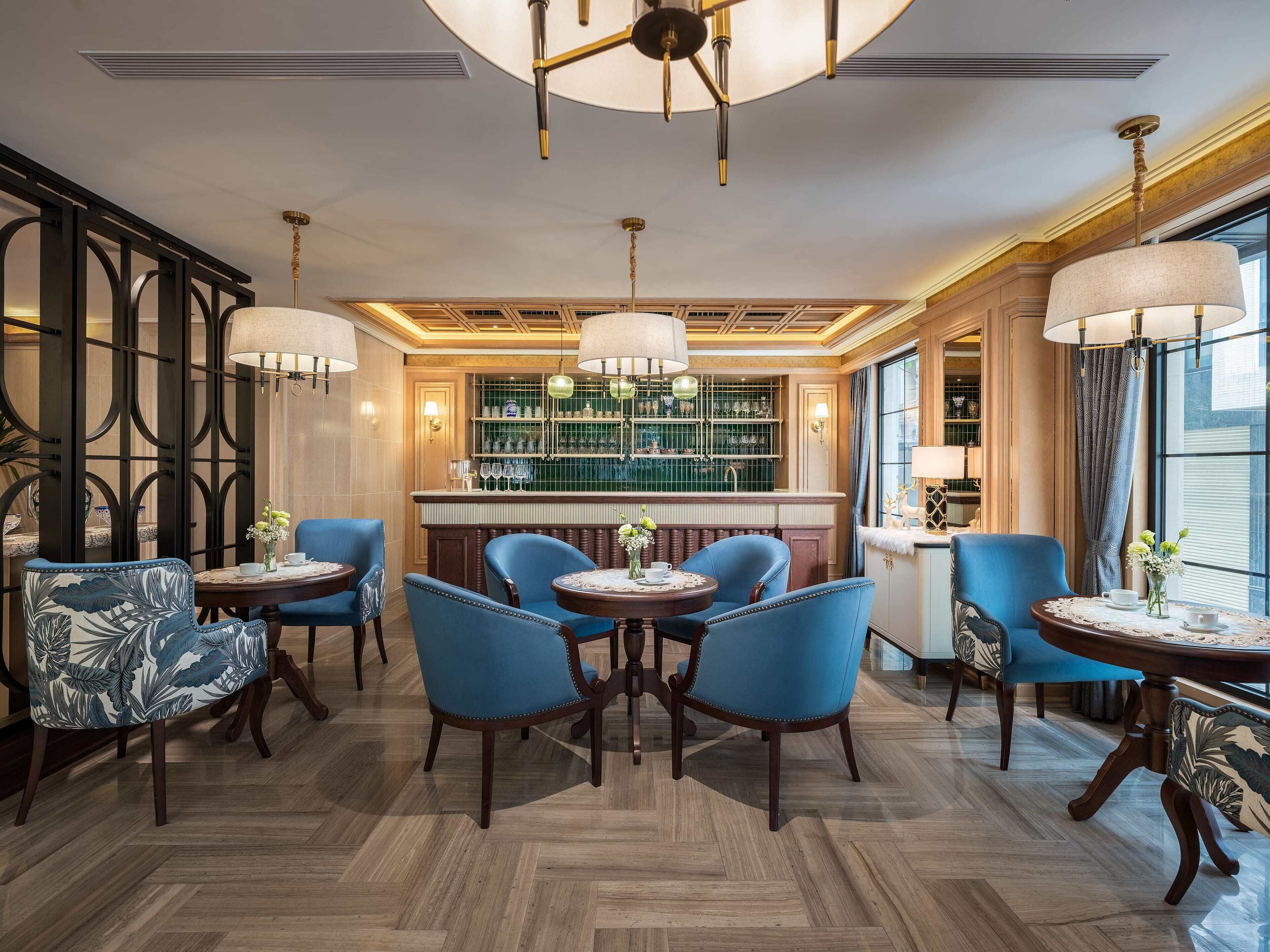 A bar area with a green-tiled wall, blue upholstered chairs, and a wooden bar counter.