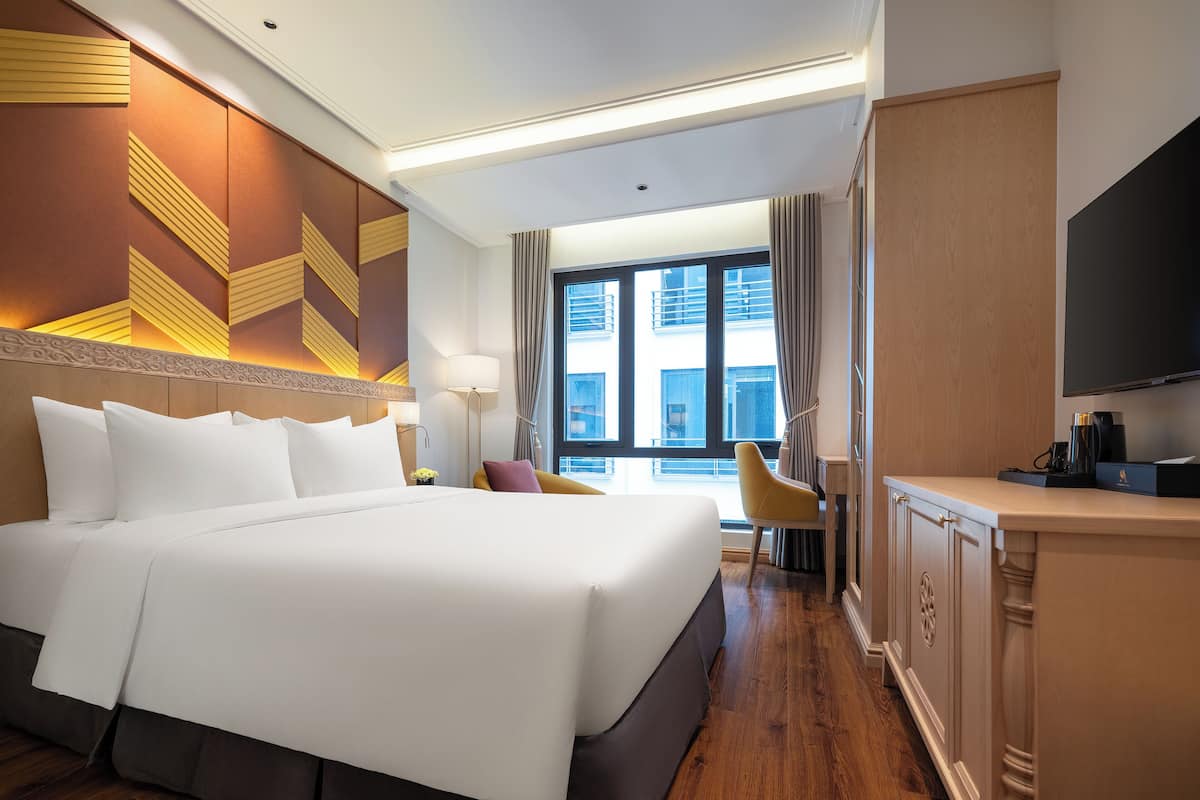 A hotel room with a large bed, a desk, a chair, and a TV.
