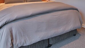A bedroom with a large bed, a nightstand, a wall-mounted shelf, and a painting.