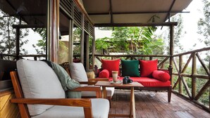 A wooden deck with a sofa and chairs, a table with a cup and camera, and a view of trees. - Nokras Enkare Luxury Tented Camp Sagana (Sagana)