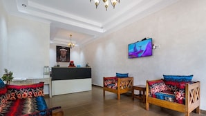 A hotel lobby with a reception desk, wooden sofas with colorful cushions, a chandelier, and a flat-screen TV on the wall. - Nokras Enkare Luxury Tented Camp Sagana (Sagana)