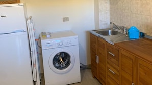 A compact kitchen with a built-in washer and dryer, wooden cabinets, a sink, and a mirror above the cabinets.