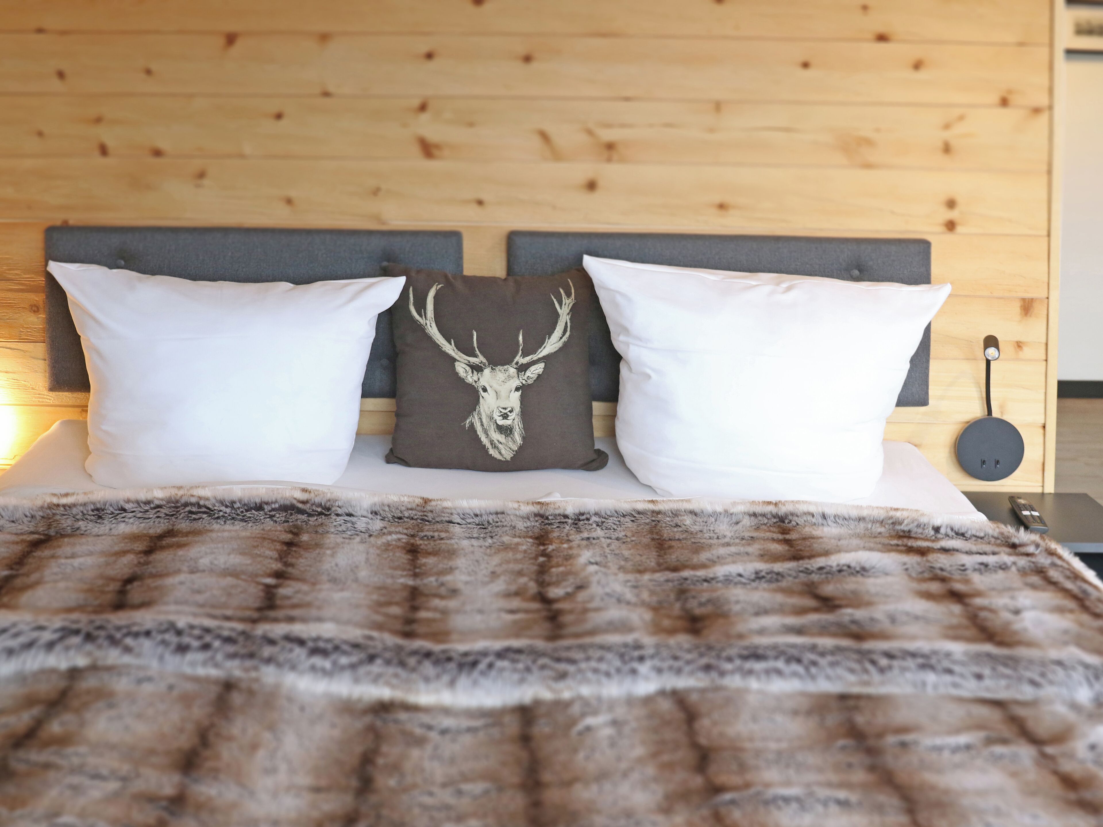 A bed with a fur throw, two white pillows, and a brown pillow with a deer head design.