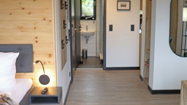 Un dormitorio moderno con cabecera de madera, una mesita de noche con lámpara y vistas al baño.