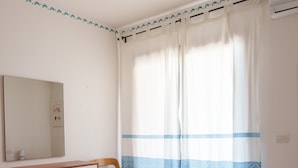 Une chambre d’hôtel avec un lit, une chaise en bois, une commode et une fenêtre avec des rideaux.