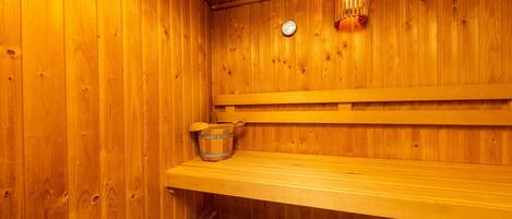 A wooden sauna with a bench, a bucket, and a wall-mounted light fixture.