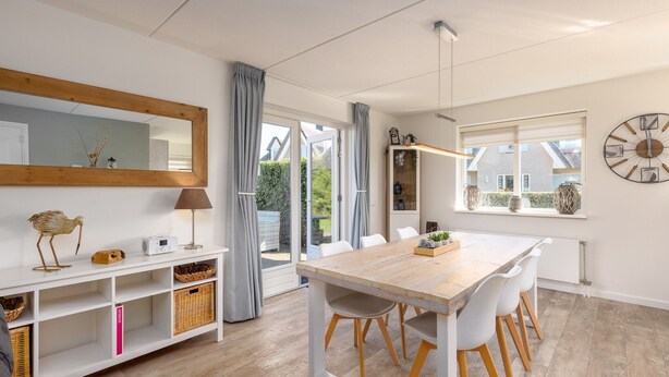 Un espace repas moderne avec une table en bois, des chaises blanches et un grand miroir au-dessus.