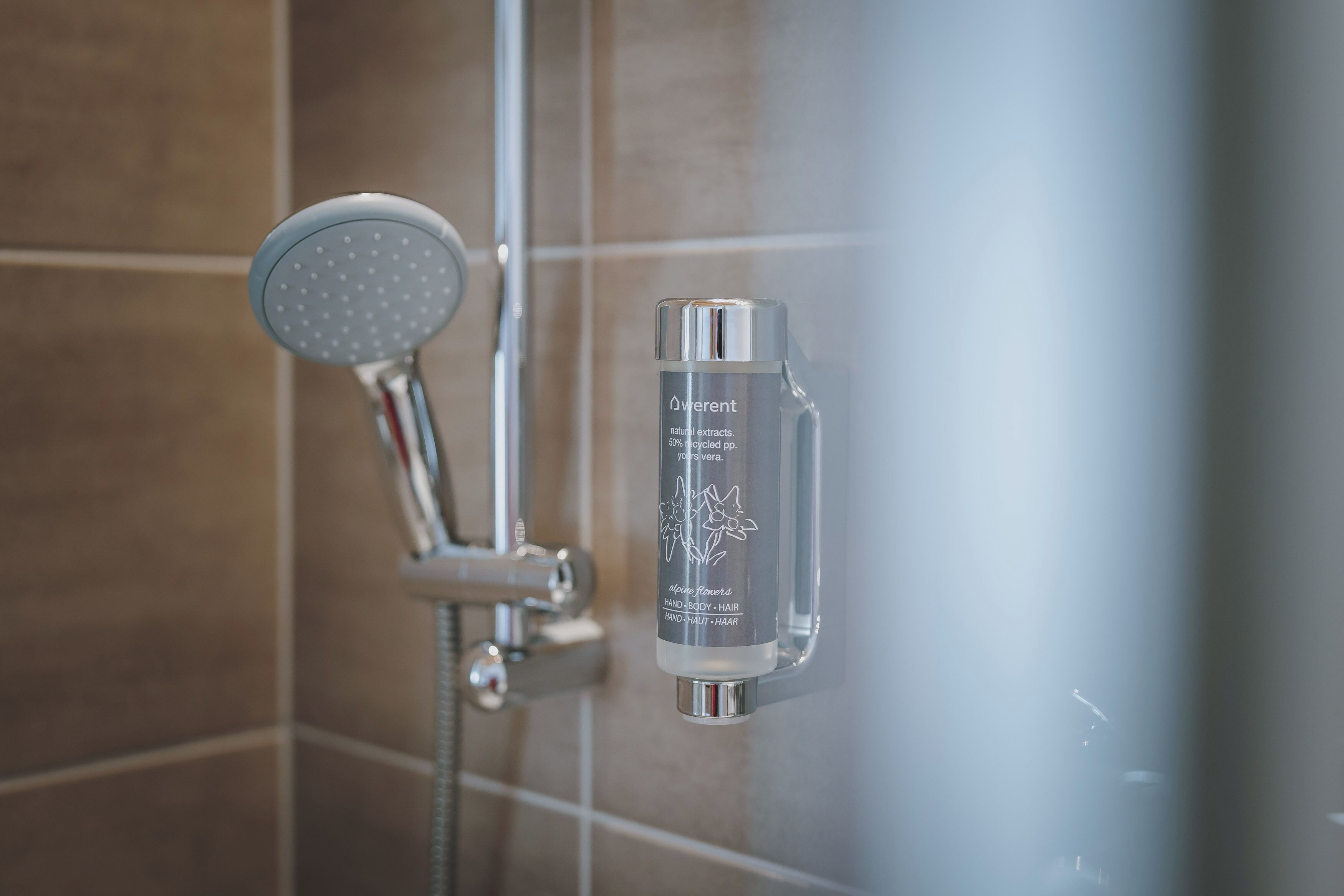 A shower with a handheld showerhead and a bottle of Aveent hand body hair product.