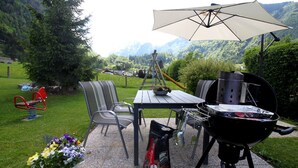 An outdoor patio with a grill, chairs, a table, and a potted plant. - Haus Katharina by we rent (Kaprun)