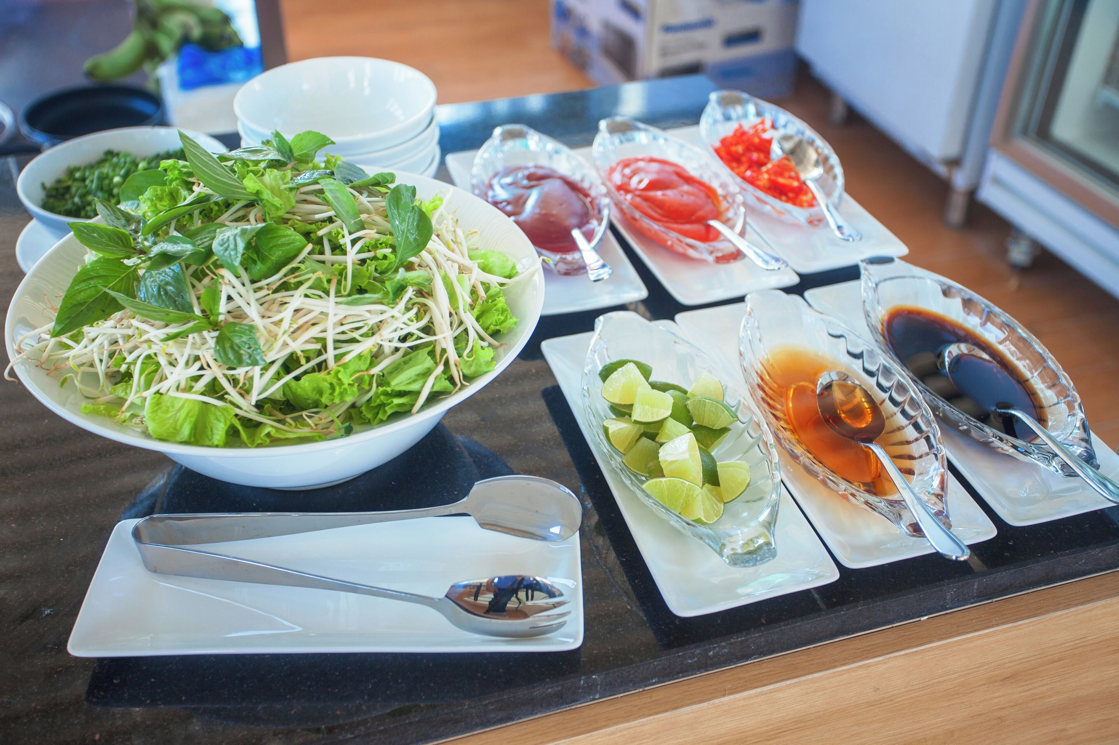 A table with various dishes including a bowl of salad, lime slices, and condiments.