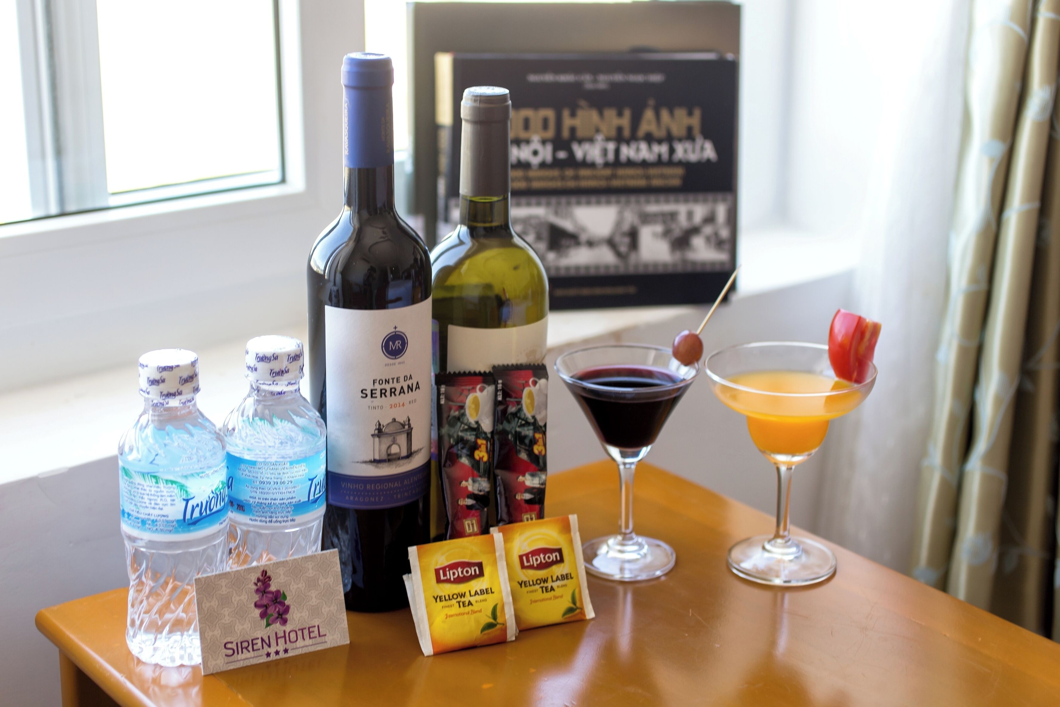 A table with bottles of water, wine, and tea, a martini glass with a cocktail, and a sign for Siren Hotel.