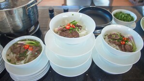 A table with several bowls of soup, a pot, and some condiments. - Siren Flower Hotel (Nha Trang)