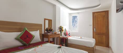 A hotel room with two beds, a wooden headboard, a desk with a mirror, a window with a view, and a wooden door.