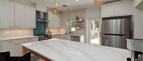 A modern kitchen with white cabinetry, a large island, stainless steel appliances, and pendant lighting.