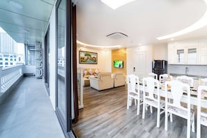 A modern kitchen with white cabinets, a dining table with chairs, a TV mounted on the wall, and a sofa in the living area.