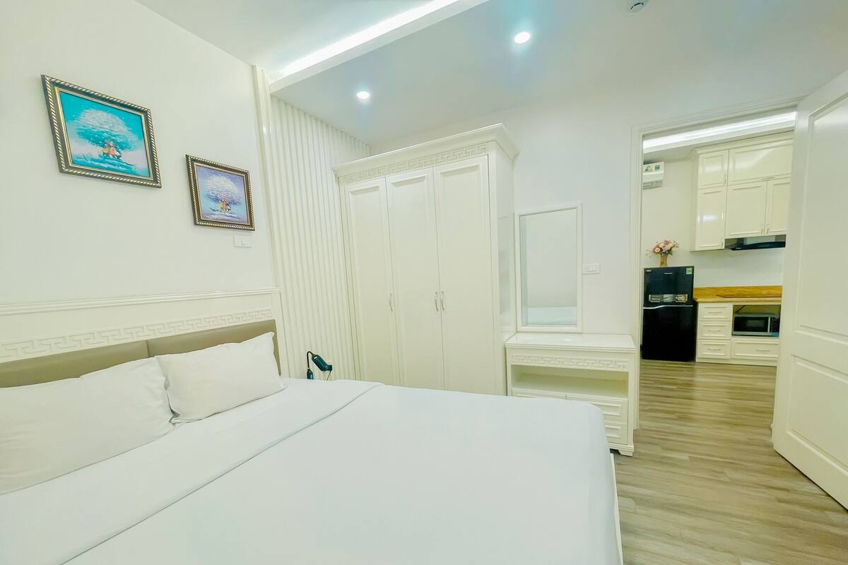 A hotel room with a large bed, a desk, a wardrobe, and a kitchenette.