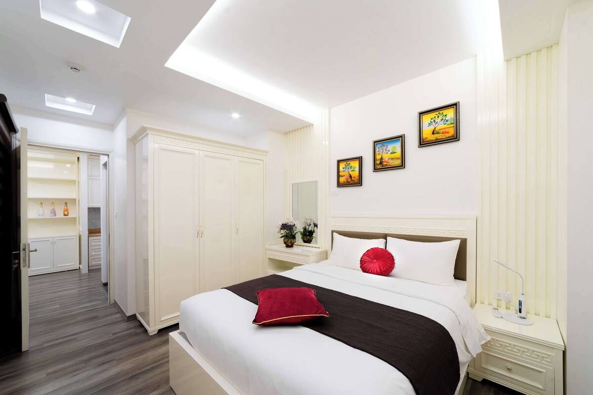 A hotel room with a large bed, a nightstand, a wardrobe, and a bathroom visible through an open door.